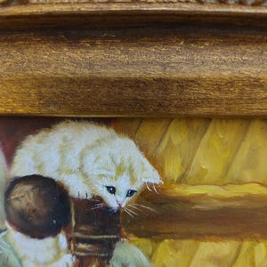 May include: A white kitten with brown markings sits on a wooden chair with a brown ball in its paws. The kitten is looking down at the ball. The background is a yellow and brown painting.
