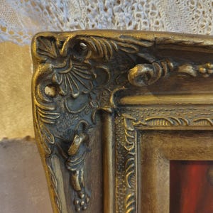 May include: Close-up of a gold-colored ornate picture frame with intricate details. The frame has a raised, textured design and a slightly worn finish.