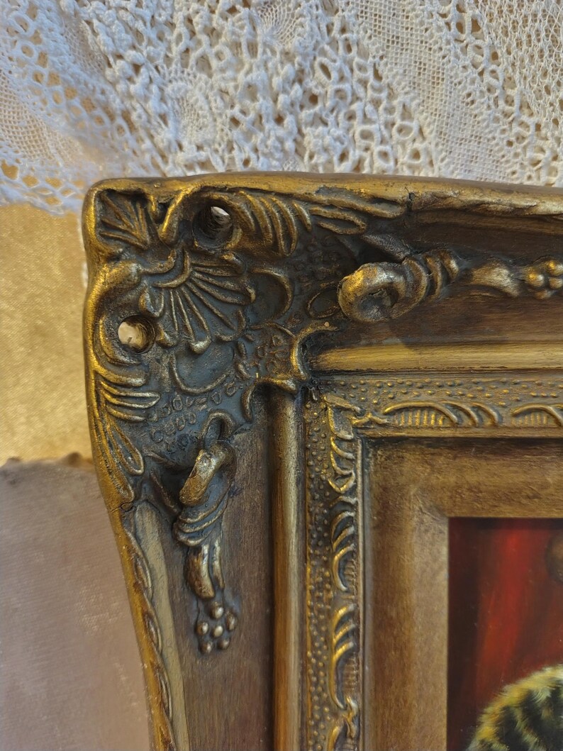 May include: Close-up of a gold-colored ornate picture frame with intricate details. The frame has a raised, textured design and a slightly worn finish.