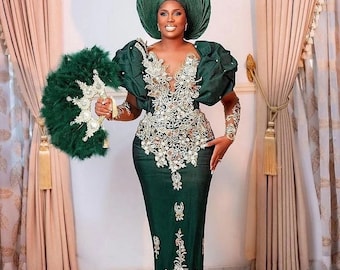 May include: A woman wearing a green dress with gold embroidery and a matching green head wrap. She is holding a green feather fan.