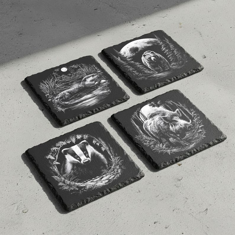 May include: Four square black slate coasters with etched wildlife designs. Each coaster features a different animal: an otter, a badger, a wild boar, and an owl. The designs are in white, set against the dark slate.