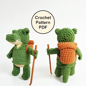 May include: Two green crochet alligator and bear figures with orange backpacks and brown walking sticks. The alligator faces forward, while the bear faces away. The text "Crochet Pattern PDF" is in a black circle.