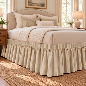 Può includere: Un letto con testiera imbottita beige e una balza con motivo a righe verticali blu, gialle e bianche. La biancheria da letto include un copriletto trapuntato color crema, due cuscini rettangolari a righe e un piccolo cuscino lombare.