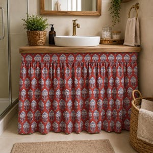 Könnte beinhalten: Ein Badezimmerschrank, der mit einem gerafften Stoffvorhang mit einem sich wiederholenden floralen Blockdruckmuster in Rot, Weiß und Blau bedeckt ist. Der Schrank hat eine Holzplatte mit einem weißen Aufsatzwaschbecken und einer Messingarmatur.