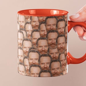 May include: A red and white ceramic coffee mug with a repeating pattern of a man's face. The mug has a red handle.