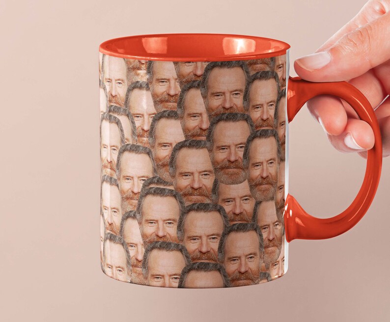 May include: A red and white ceramic coffee mug with a repeating pattern of a man's face. The mug has a red handle.