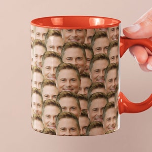 May include: A red and white ceramic coffee mug with a pattern of a man's face repeated all over the mug.