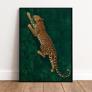 Pode incluir: Uma impressão de arte emoldurada apresentando um leopardo com pelagem dourada e manchas pretas subindo contra um fundo verde escuro sólido. O leopardo está posicionado na diagonal, mostrando o corpo inteiro, a cauda e as patas estendidas.