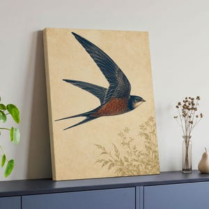 May include: A rectangular canvas print featuring a detailed illustration of a swallow in flight. The bird has dark blue wings and a reddish-brown chest. Below the bird, faint gold-toned botanical line drawings are set against a beige background.
