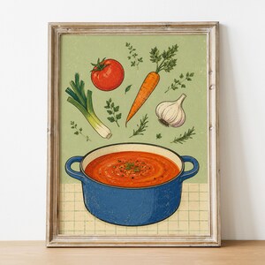 May include: A framed wall art print featuring a blue pot filled with orange soup. Above the pot are illustrations of a red tomato, an orange carrot, a white garlic bulb, a green leek, and various green herbs against a light green background.