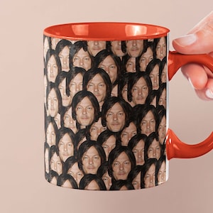 May include: A white ceramic coffee mug with an orange rim and handle. The mug features a repeating pattern of a man's face.