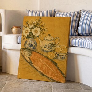 May include: A rectangular canvas print featuring a still life illustration on a mustard yellow background. The artwork depicts a whole salmon, a blue and white floral vase with white flowers, a matching teapot, and a bowl filled with sliced oranges.