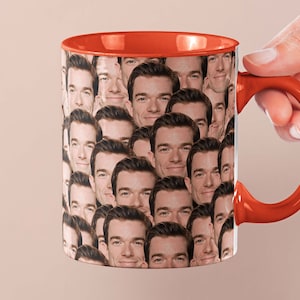 May include: A red coffee mug with a pattern of a man's face repeated all over the mug.