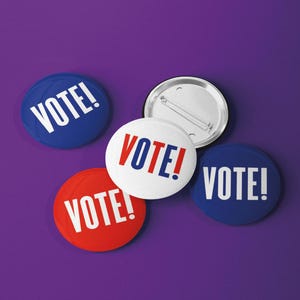 May include: Four circular pin-back buttons featuring the word VOTE! in bold white or red and blue lettering. Two buttons are blue, one is red, and one is white. One button is flipped over to show the silver metal backing and pin mechanism.