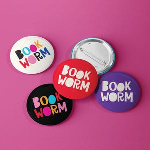 May include: Four round pins with the words "Book Worm" in different colors. The pins are white, red, black, and purple.
