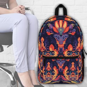 May include: A backpack featuring a symmetrical floral design in orange, purple, and yellow on a dark blue backdrop. It has a front pocket and a black handle. The design is intricate.