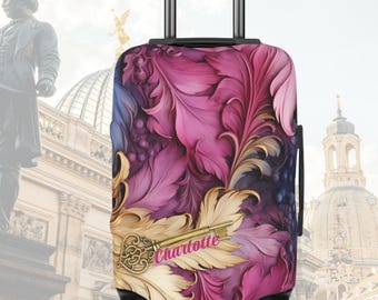 May include: A rolling suitcase featuring a vibrant pattern of magenta, purple, and cream-colored feathers. A gold-toned ornate key is positioned horizontally across the lower section, with the name Charlotte printed in pink script over the key.