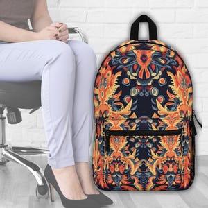 May include: A backpack featuring a detailed, symmetrical pattern in orange, blue, and yellow on a dark base. It has a black top handle, a front zip pocket, and black mesh side pockets. The design is intricate and eye-catching.