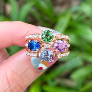 May include: A multi-stone ring crafted in rose gold featuring a round green gemstone, a round blue gemstone, a round pink gemstone, and a cushion-cut light blue gemstone, accented with small white diamonds along the band and a central diamond.
