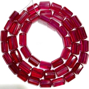 May include: A strand of deep red, translucent, cylindrical beads with faceted surfaces. The beads are arranged in a circular pattern, strung together on a thin, light-colored thread, showcasing a uniform shape and a vibrant, glossy finish.
