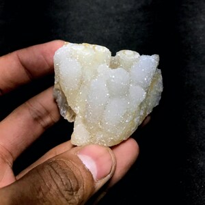 May include: A white and cream colored crystal cluster with a rough, textured surface. The crystal has a heart-like shape and is composed of many small, white crystals.
