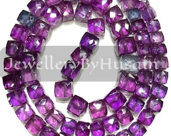 May include: A strand of faceted, square-cut amethyst beads in varying shades of purple. The beads are strung together, creating a necklace or bracelet. The text "JewelleryByHusain" is visible.