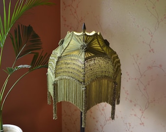 May include: A green lampshade with a fringe design. The lampshade is made of a woven material and has a geometric pattern.
