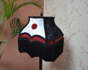 May include: A black and white lampshade with red trim and a red flower design. The lampshade has a fringe around the bottom.