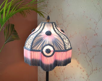 May include: A pink and black lampshade with a fringe trim. The lampshade has a floral pattern and a beaded design.
