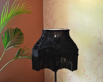 Può includere: Un paralume nero con un bordo a frangia e un design decorativo. Il paralume è realizzato in tessuto intrecciato e ha una forma quadrata.
