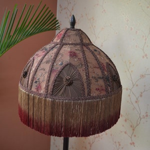 Op de afbeelding: Een vintage lampenkap met een bruin en roze bloemenpatroon, een franje rand en een donkerbruine bovenkant.
