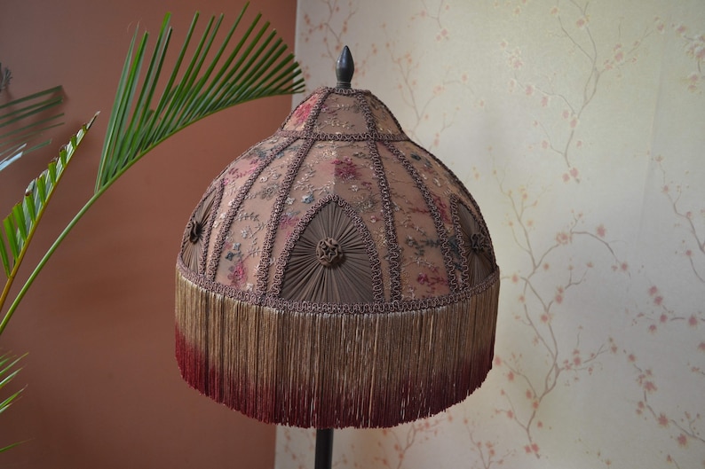 Op de afbeelding: Een vintage lampenkap met een bruin en roze bloemenpatroon, een franje rand en een donkerbruine bovenkant.