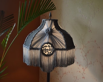 May include: A black and white lampshade with a fringe trim. The lampshade has a geometric pattern and a black and white floral design in the center.
