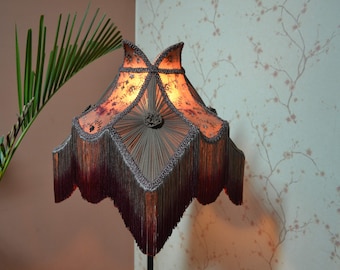 Könnte beinhalten: Ein Lampenschirm im Vintage-Stil mit einem Fransenrand und einem Blumenmuster. Der Lampenschirm ist aus weichem Stoff gefertigt und hat ein warmes, einladendes Leuchten.