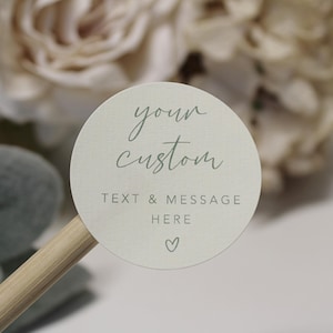 May include: A round, cream-coloured sticker with the text "your custom text & message here" in grey script font. A small heart is below the text.