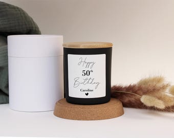 Puede incluir: Vela negra con tapa de madera y una etiqueta blanca que dice "Happy 50th Birthday Caroline" con un pequeño corazón.