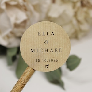 Könnte beinhalten: Ein runder, brauner Papiersticker mit dem Text "Ella & Michael 15.10.2026" und einem kleinen Herzsymbol.