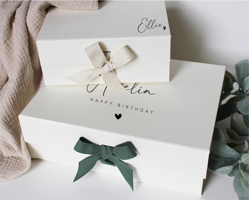 Op de afbeelding: Twee witte cadeaudozen met een groene strik op de onderste doos. De bovenste doos heeft de naam "Ellie" erop staan. De onderste doos heeft de naam "Olivia" en de tekst "Happy Birthday" erop staan.