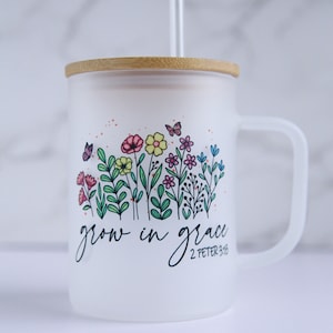 May include: White ceramic mug with a bamboo lid and a straw. The mug has a floral design with butterflies and the text "grow in grace 2 Peter 3:18".