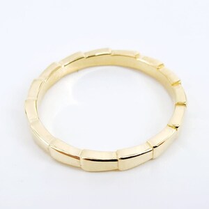 May include: A gold band ring with a unique, textured design. The band is made up of a series of small, rectangular shapes.