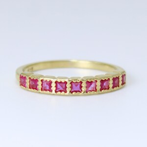 May include: A gold band ring with a row of pink square-shaped gemstones.