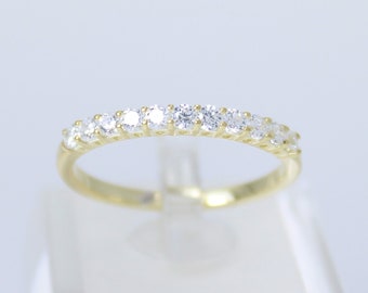 May include: A gold band ring with a row of small, clear round stones.