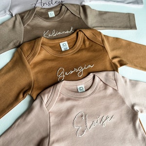 Hand Embroidered long sleeve baby onesies with names hand embroidered across the chest.