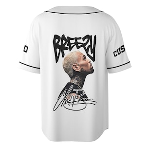May include: White baseball jersey with black trim and the word "Breezy" in a black, stylized font on the back. A portrait of a person with blonde hair and tattoos is featured below the text, along with a signature.