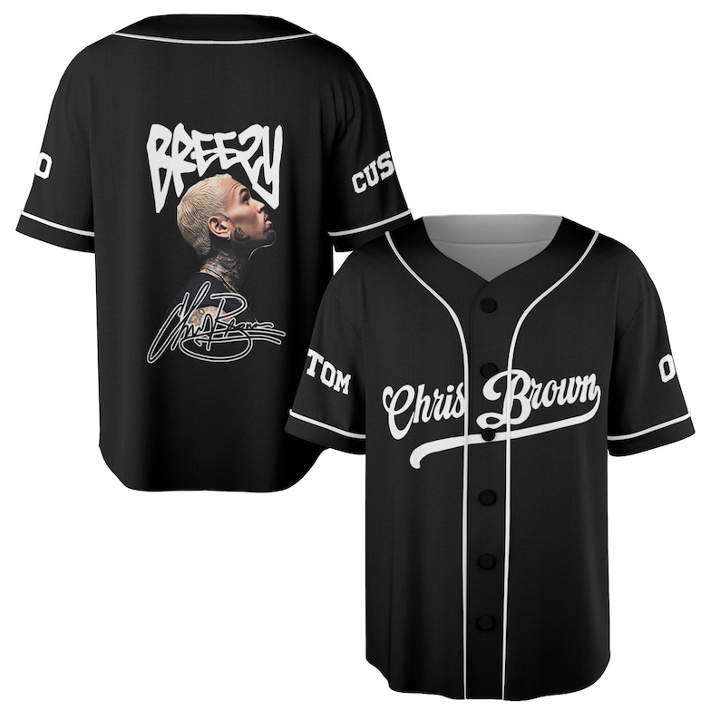 May include: Black baseball jersey with white trim and buttons. The front features the text "Chris Brown" in a cursive font. The back displays the word "Breezy" above a portrait and signature. The jersey has short sleeves and a button-down front.