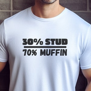 May include: White t-shirt with the text "30% STUD 70% MUFFIN" in black. The shirt is short-sleeved and has a crew neck. A white circle with the word "WHITE" is in the lower right corner.