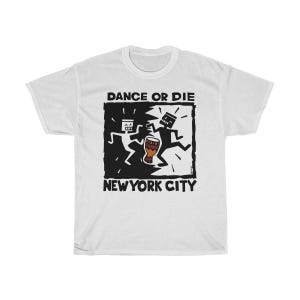 Puede incluir: Camiseta blanca con un gráfico en blanco y negro. El gráfico presenta dos figuras de palo bailando con un tambor, sobre un fondo en blanco y negro. El texto en la camiseta dice "DANCE OR DIE" y "NEW YORK CITY."