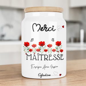 Peut inclure: Un bocal de rangement en céramique blanche avec un couvercle en bois clair, orné de coquelicots rouges, de papillons et de coccinelles. Le texte indique Merci MAÎTRESSE Enseigner Aimer Inspirer Eglantine en lettres noires.
