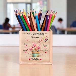 Peut inclure: Un pot à crayons en bois rempli de crayons de couleur. Le pot est décoré d'un motif floral et du texte "Ma Super Maîtresse Merci pour..." et d'autres mots. Un cadeau de Saint-Valentin.
