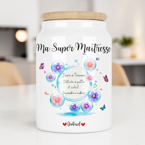 Peut inclure: Un bocal de rangement en céramique blanche avec un couvercle en bois clair. L'avant présente le texte "Ma Super Maitresse" au-dessus d'une bulle centrale contenant du texte, entourée de bulles florales colorées, de papillons et du nom "Gabriel".